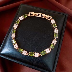 Detailed close-up of 18k gold plated bracelet with green zircons on a black leather box