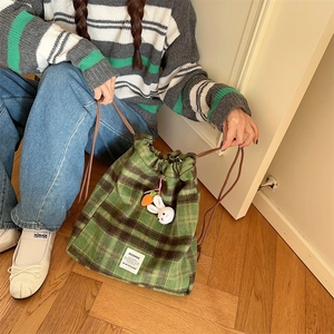Close-up of green plaid wool backpack with drawstring closure and cute knit rabbit charm
