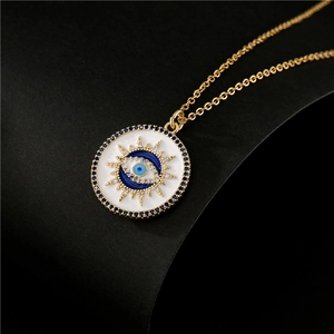 Gold evil eye necklace with white enamel and blue crystals on a dark background
