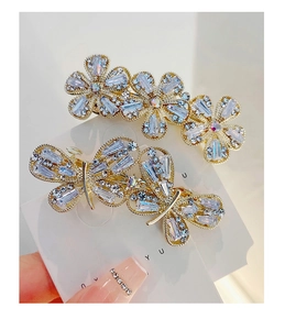 Detailed macro view of two gold-plated hair clips with inlaid crystals and flower shapes