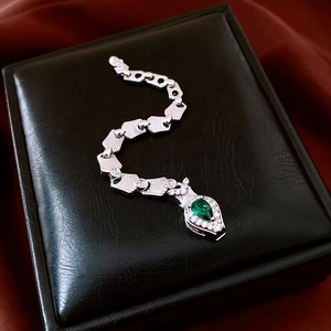 Detailed macro view of silver snake-shaped bracelet with green pear gemstone on black leather