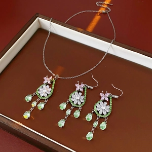 Dettaglio macro di collana e orecchini in argento con fiori e farfalle in pietre preziose