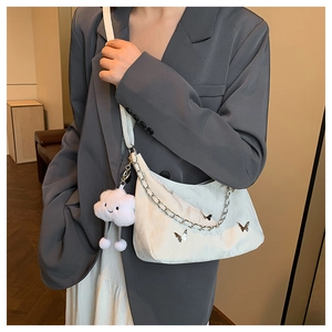 Detail of white nylon shoulder bag with silver chain, butterfly decor and plush charm