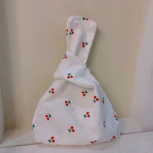 Close-up of Japanese knot bag in white fabric with red cherry pattern and jacquard texture