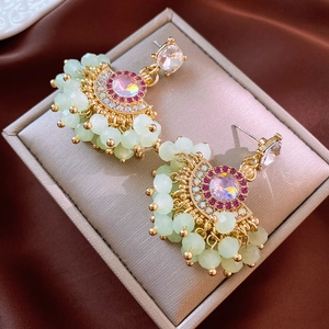 Detail view of gold fan-shaped earrings with light green beads and pink rhinestones