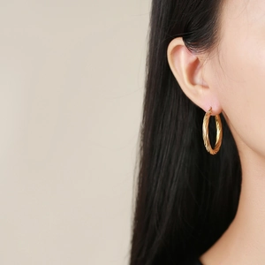 Close-up of elegant gold twisted rope hoop earrings worn on a model with a minimalist style