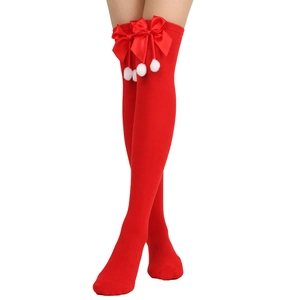 Detail of red cable knit over-knee socks featuring satin bows and white fuzzy pom-poms