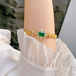 Detail of luxury braided gold bracelet with emerald green gem and white diamonds