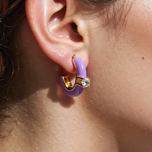 Close-up of a purple C-shaped earring with gold base and zircon stone on model