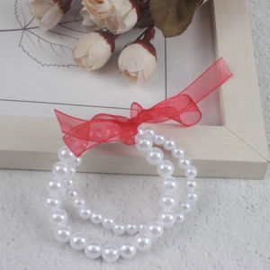 Detail of white faux pearl bracelet for girls featuring a red organza bow on textured surface