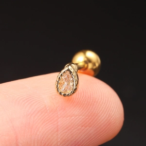 Macro shot of gold teardrop zircon ear stud on fingertip showing detailed screw ball back