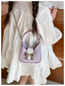 Rear view of a lavender and white PU crossbody bag with metal bow on a white dress