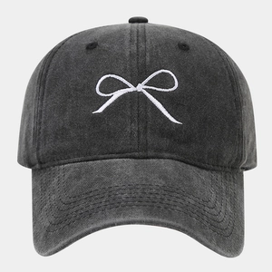 Close-up of white bow embroidery and washed dark gray cotton fabric on baseball cap