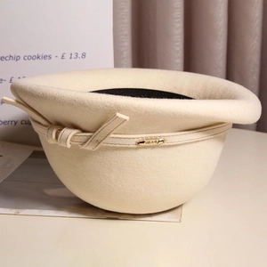 Detail of off-white wool beret featuring a delicate leather band and gold metal tag
