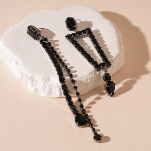 Detail of dark style asymmetric earrings with black crystals and long fringe on stone