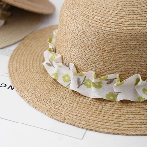 Close-up of woven straw hat featuring floral chiffon ribbon and frilled trim details