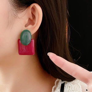 Macro view of geometric green oval and red square resin earrings on model's ear