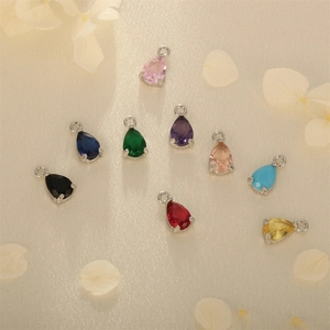 Colorful pear-shaped zircon pendants with silver metal base on elegant fabric background