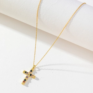 Detail of gold-plated cross pendant with colorful zircon stones on white display