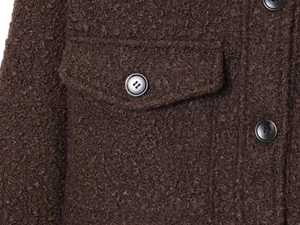 Détail macro du tissu texturé marron foncé avec poche et boutons en résine sur la veste