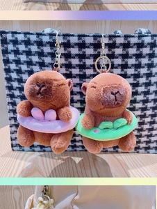 Detail of plush capybara keychains with pink and green swim rings on a checkered bag