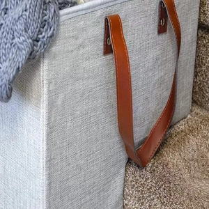 Detail of grey fabric staircase basket with reinforced leather handles on carpeted stairs
