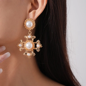 Detailed close-up of a vintage golden cross earring with inlaid pearls on a model