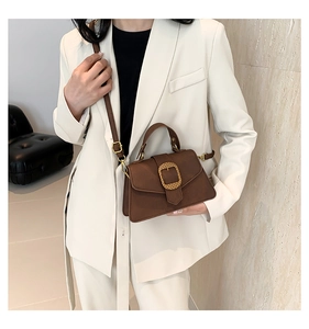 Brown faux suede crossbody bag with gold buckle worn by a model in a beige suit