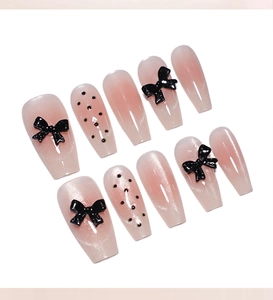 Detailed view of pink cat-eye press-on nails with 3D black bows and polka dot accents