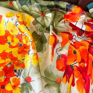 Floral print silk scarf with bright orange and green patterns on smooth satin fabric