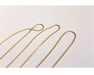 Macro detail of three thin gold snake chains with polished metallic finish on white