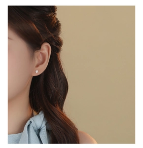 Close-up of minimalist S999 sterling silver flower stud earring worn by a model