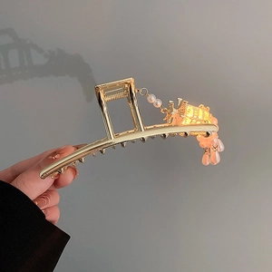 Detailed view of a golden vintage hair claw clip with pearl and pink bead tassels