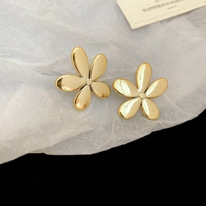 Vue détaillée de boucles d'oreilles fleur dorée sur papier crépon blanc et fond noir