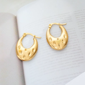 Detail of 18K gold plated oval teardrop earrings with irregular dot texture on white paper
