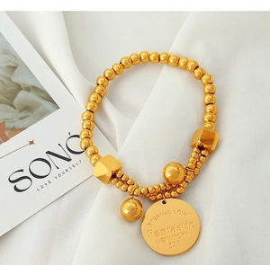 Macro detail of 18k gold bead bracelet with engraved eternal love coin and cube charms