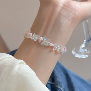 Close-up of iridescent acrylic butterfly charms and pearls on a pink braided rope bracelet