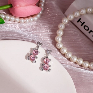 Vue détaillée de boucles d'oreilles ours rose avec cristaux sur fond de soie