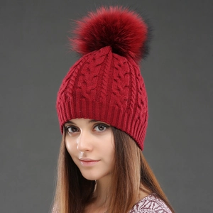Detailed close-up of wine red cable knit beanie texture with fluffy raccoon fur pom-pom