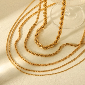 Detailed close-up of various gold-tone twisted rope necklaces on a textured beige surface