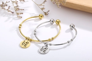 Detail of gold and silver open bangles with LOVE heart pendants on a wooden tray