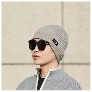 Detail of light gray ribbed knit beanie with a black square logo patch for men