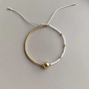 Detail of adjustable pearl bracelet with gold beads and a woven cord closure