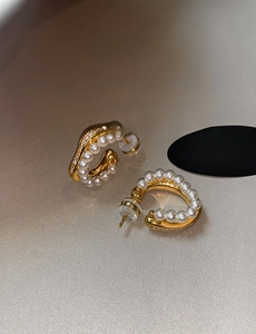 Detail of C-shaped gold pearl earrings with shimmering pavé crystal accents