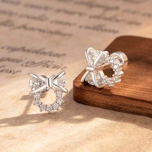 Silver bowknot earrings with cubic zirconia stones displayed on vintage paper backdrop