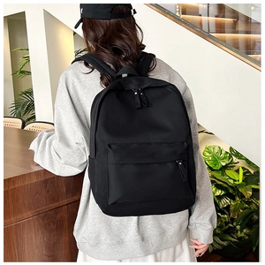 Rear view of a model wearing a black lightweight nylon backpack in a modern interior