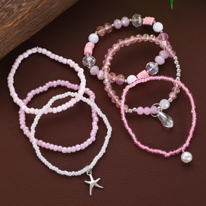 Dettaglio di bracciali multistrato con perline rosa e ciondoli a stella marina e cristallo