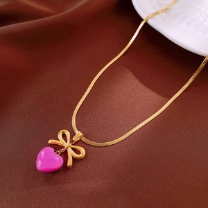 Détail du collier chaîne serpent dorée avec pendentif cœur rose et nœud sur soie
