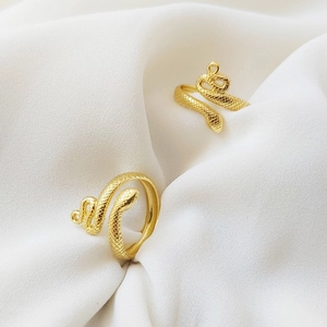Macro shot of gold snake rings with scale texture resting on elegant white silk fabric