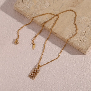 Macro detail of gold necklace featuring a hollow rectangular pendant with zircons